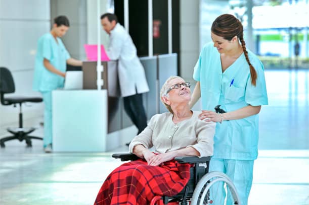 A senior citizen in a wheelchair being pushed by a hospital staff