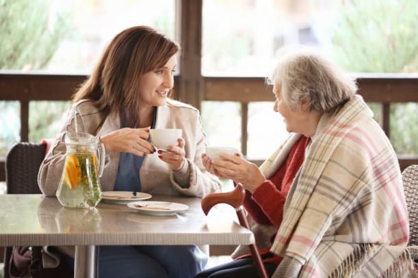 A caregiver and an old lady having tea together