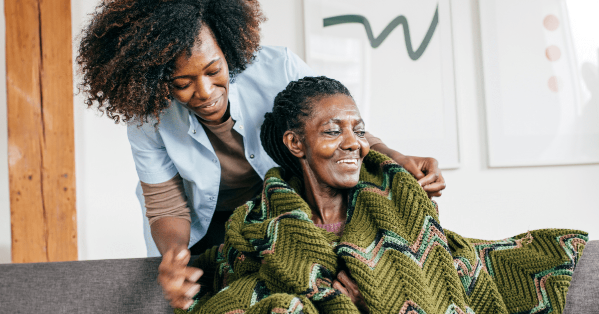 A caregiver placing a blanket on the shoulder of a woman